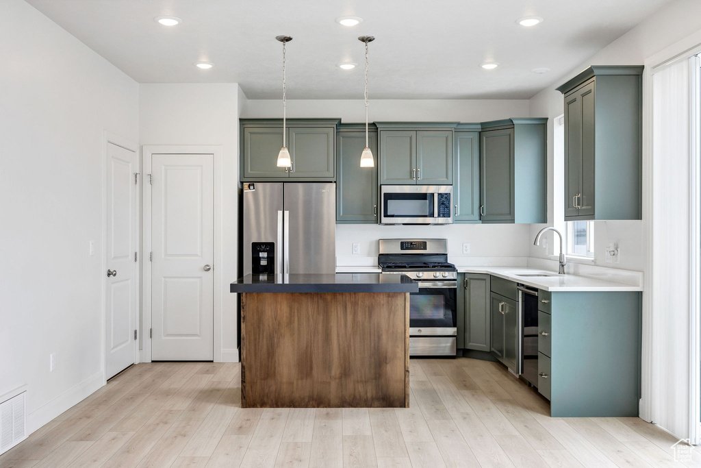 Kitchen featuring light wood-type flooring, stainless steel appliances, a center island, hanging light fixtures, and a sink