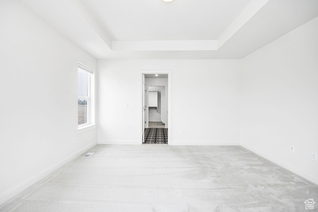 Empty room with carpet flooring, a raised ceiling, baseboards, and visible vents