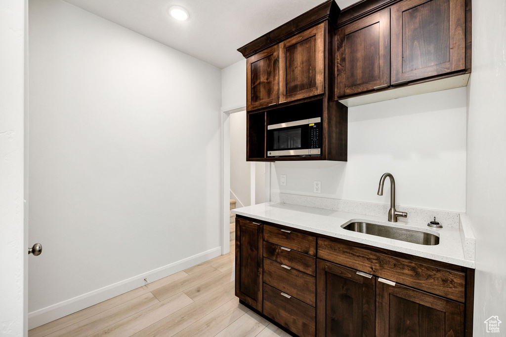 Kitchen with dark brown cabinetry, a sink, light wood finished floors, stainless steel microwave, and baseboards