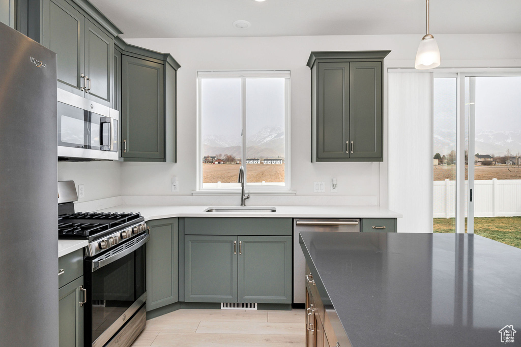Kitchen with a sink, appliances with stainless steel finishes, hanging light fixtures, light wood-style flooring, and visible vents