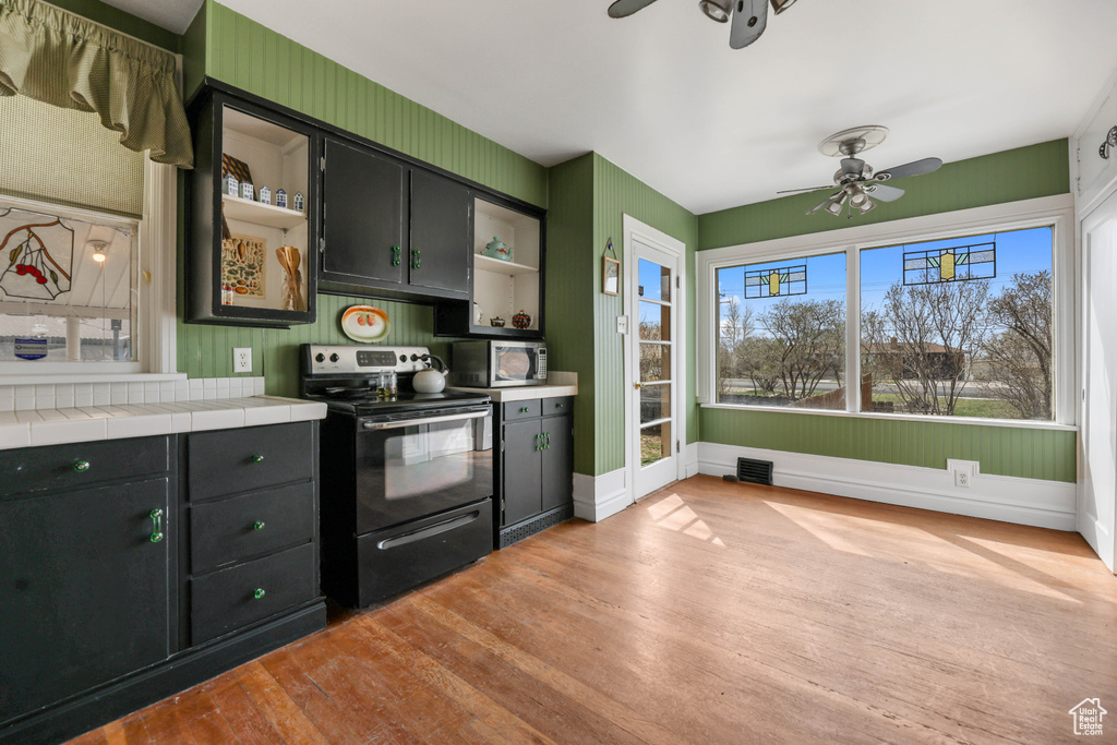 Kitchen with black electric range oven, light wood-style flooring, open shelves, stainless steel microwave, and a ceiling fan
