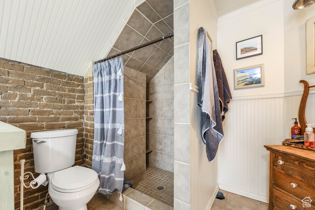 Bathroom with a wainscoted wall, a tile shower, toilet, vanity, and tile patterned flooring