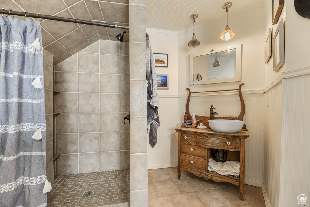 Bathroom with tile patterned floors, tiled shower, vanity, wainscoting, and ornamental molding