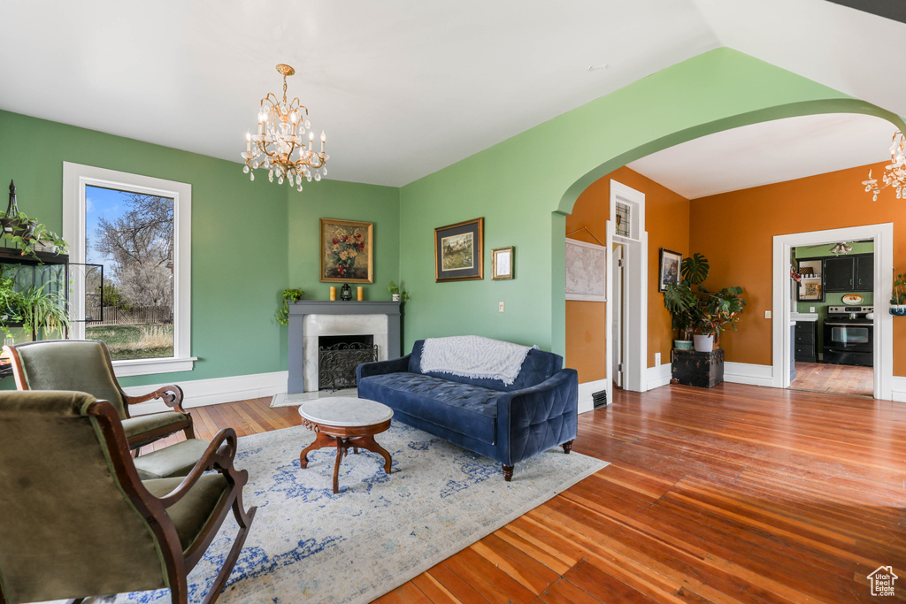Living area with a notable chandelier, wood finished floors, a premium fireplace, baseboards, and arched walkways