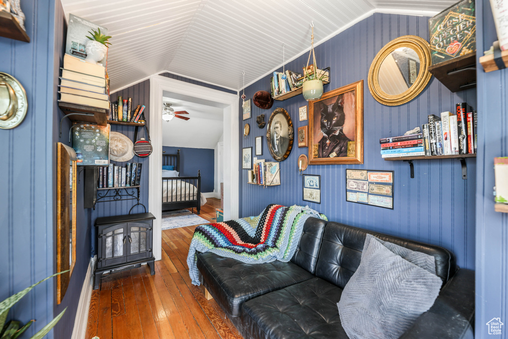 Living room with vaulted ceiling, ceiling fan, hardwood / wood-style flooring, and a wood stove