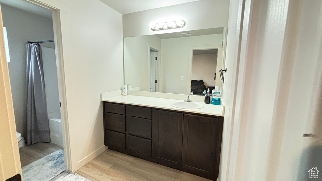 Ensuite bathroom featuring vanity, shower / bathtub combination with curtain, toilet, connected bathroom, and wood finished floors
