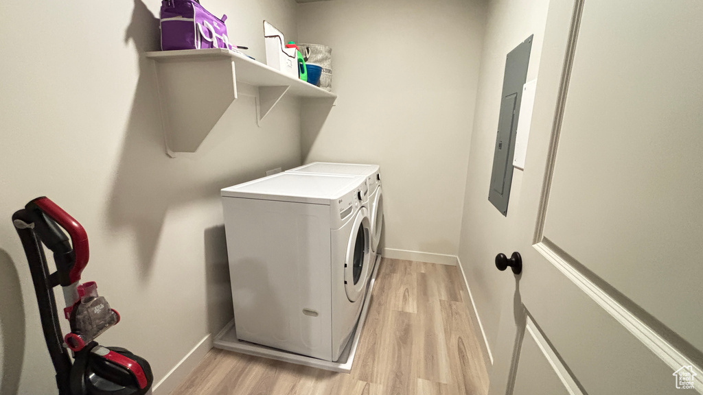 Washroom featuring washing machine and clothes dryer, light wood-style flooring, electric panel, baseboards, and laundry area