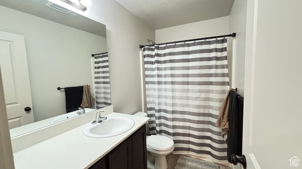 Bathroom with a textured ceiling, visible vents, toilet, vanity, and a shower with curtain