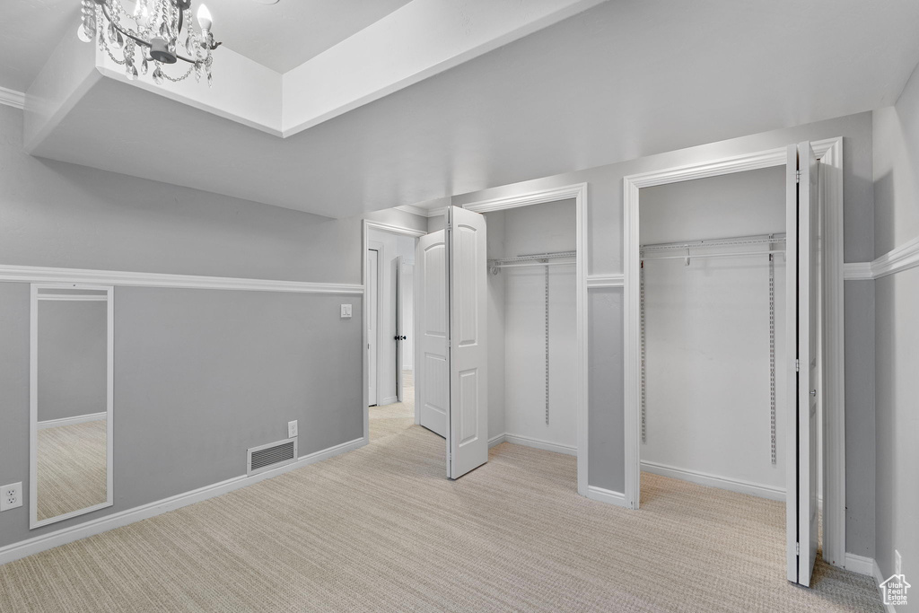 Unfurnished bedroom with two closets, carpet flooring, a chandelier, and baseboards