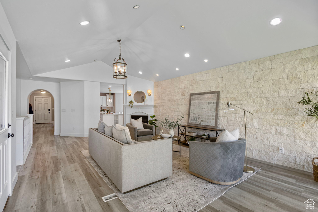 Living area with arched walkways, lofted ceiling, light wood-style floors, a chandelier, and recessed lighting