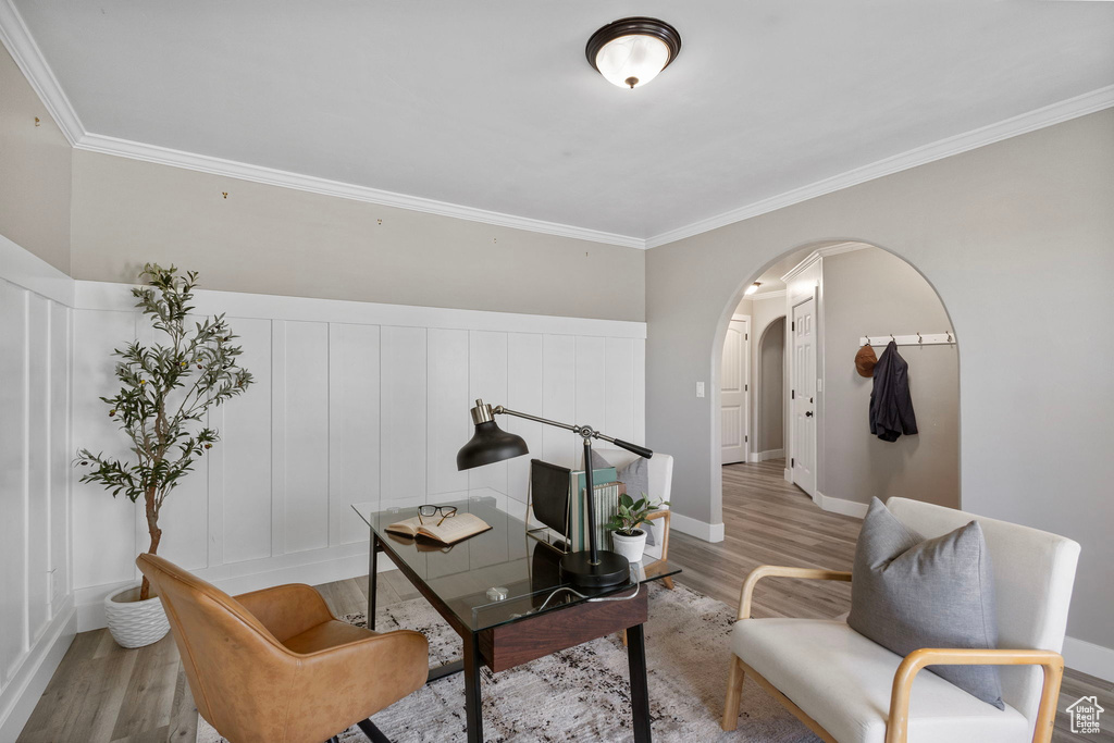 Living area featuring arched walkways, light wood-style flooring, ornamental molding, and baseboards