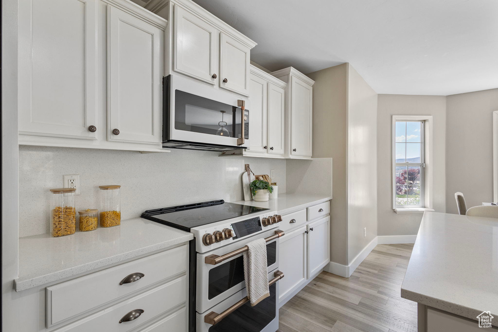 Kitchen with white appliances, white cabinetry, light wood-style flooring, and baseboards