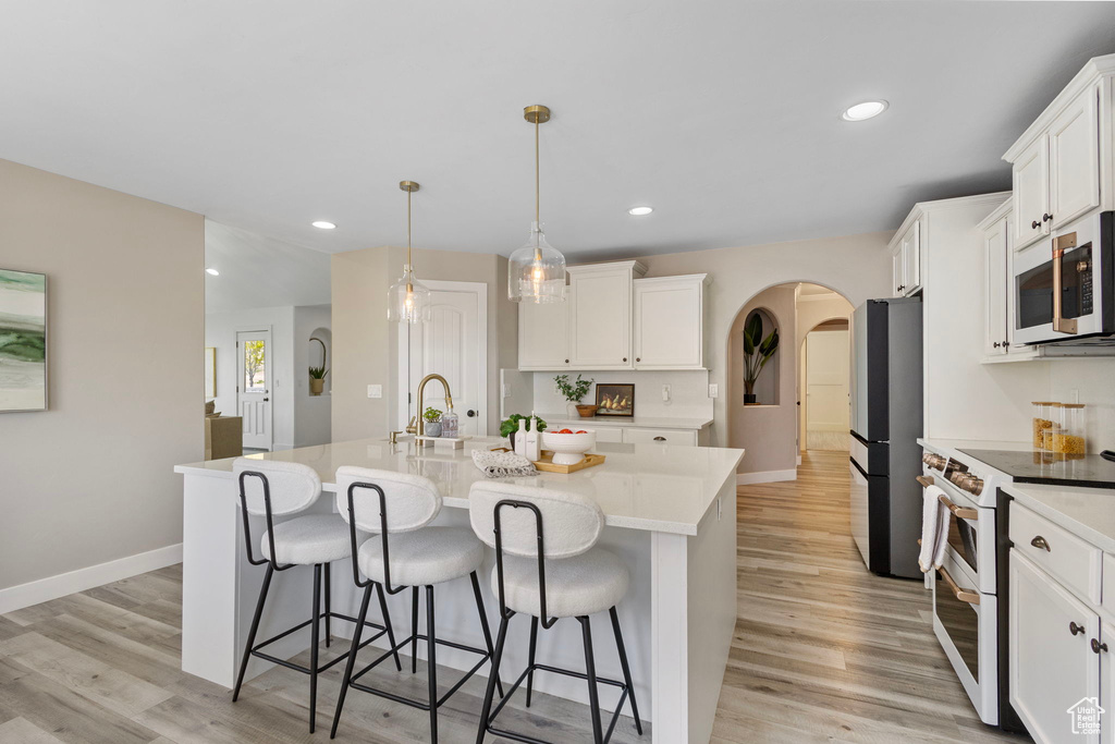 Kitchen featuring white appliances, arched walkways, a kitchen breakfast bar, white cabinetry, and light countertops