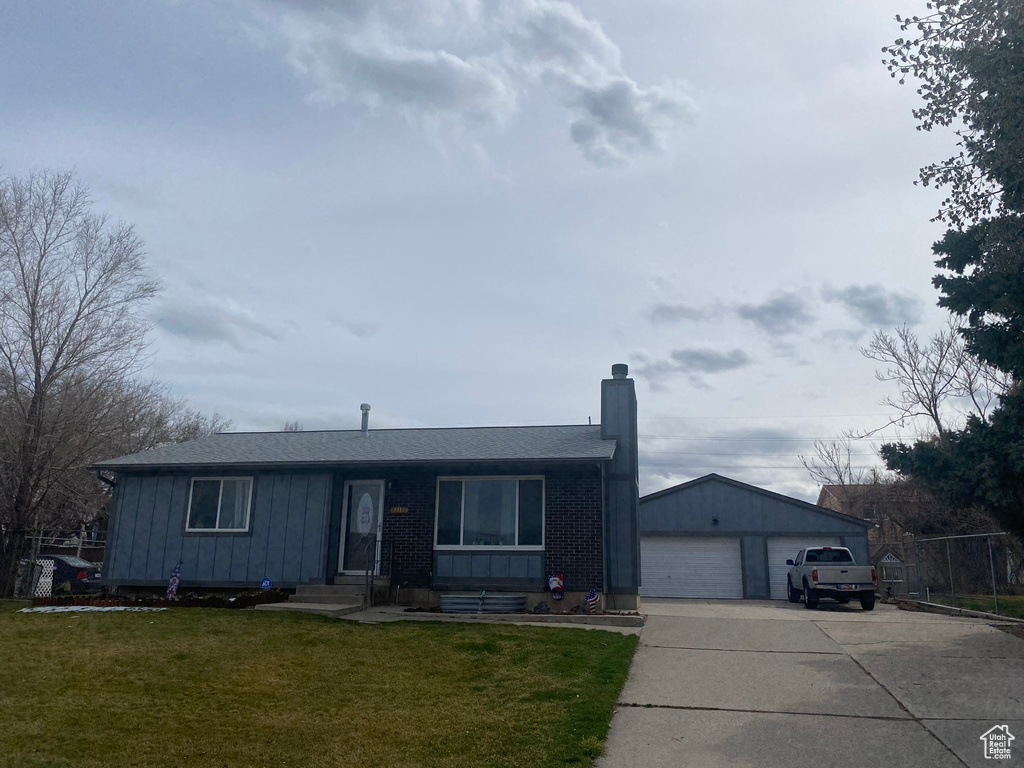 Ranch-style house with an outdoor structure, board and batten siding, a detached garage, a front lawn, and a chimney