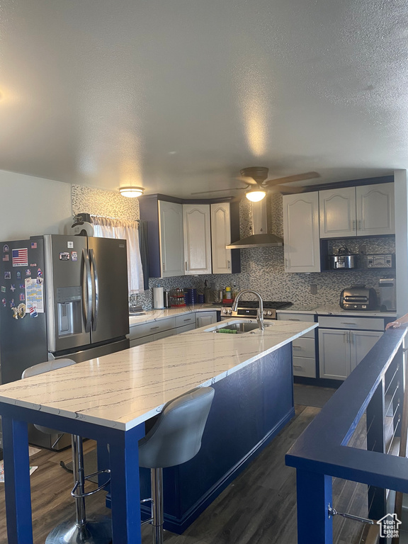 Kitchen featuring wall chimney range hood, backsplash, dark wood-type flooring, and stainless steel refrigerator with ice dispenser