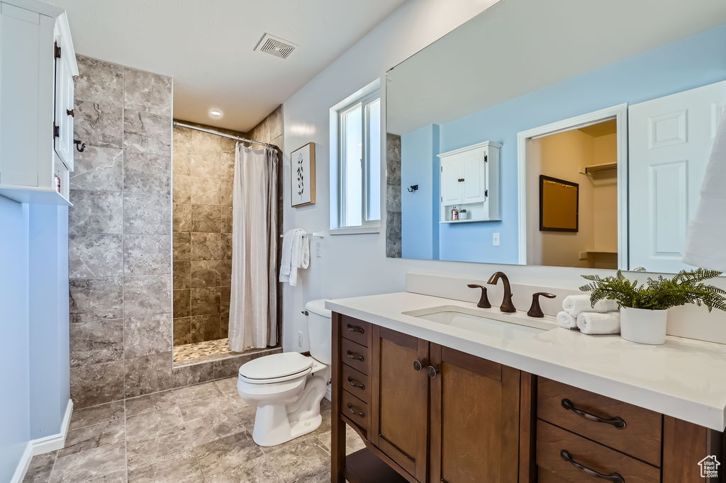 Bathroom with toilet, vanity, tiled shower, and visible vents