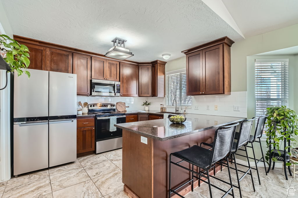 Kitchen with a breakfast bar area, decorative backsplash, dark stone counters, a sink, and appliances with stainless steel finishes