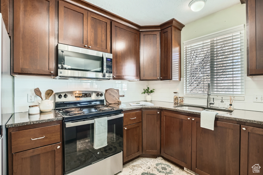 Kitchen featuring dark stone countertops, a sink, tasteful backsplash, and appliances with stainless steel finishes