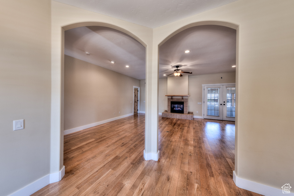 Unfurnished living room featuring baseboards, wood finished floors, a glass covered fireplace, and a ceiling fan