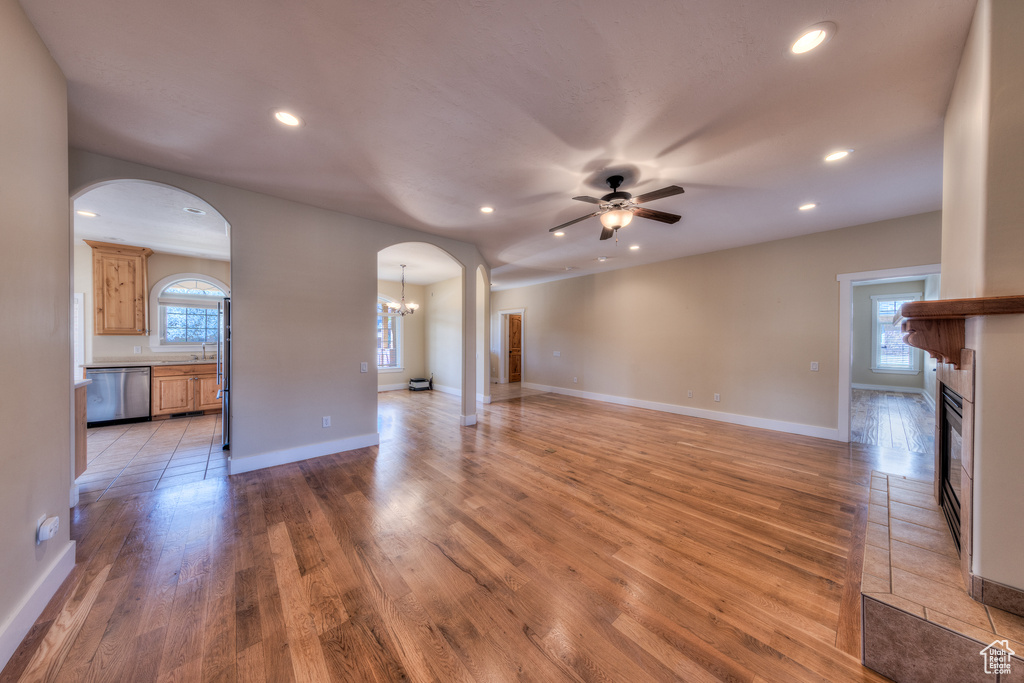 Unfurnished living room featuring recessed lighting, light wood-type flooring, ceiling fan with notable chandelier, arched walkways, and a glass covered fireplace