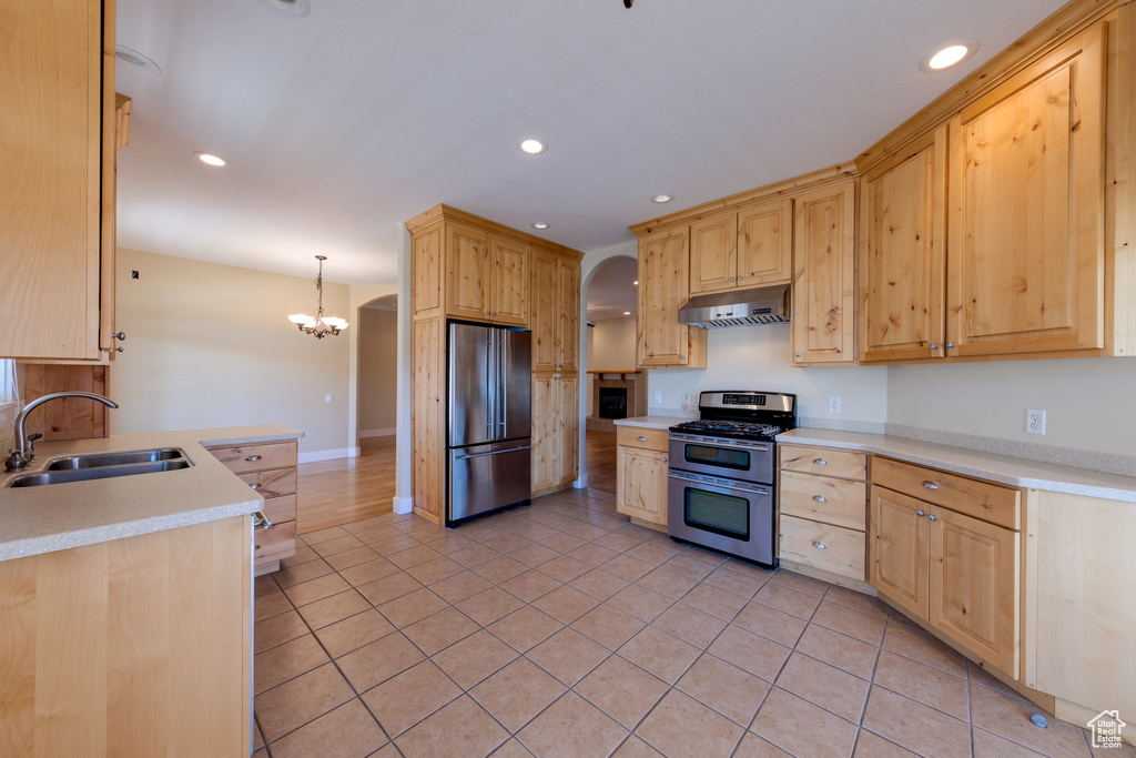 Kitchen featuring stainless steel appliances, light brown cabinets, under cabinet range hood, arched walkways, and a sink