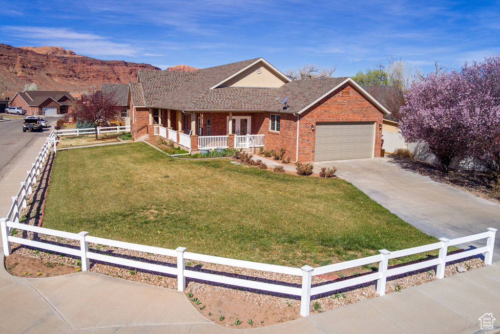 Ranch-style house featuring fence, driveway, a front lawn, covered porch, and brick siding