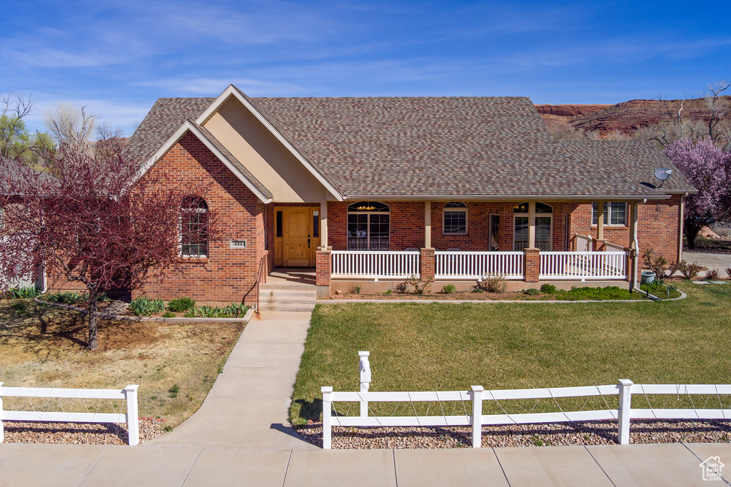Single story home featuring covered porch, a front lawn, brick siding, and roof with shingles