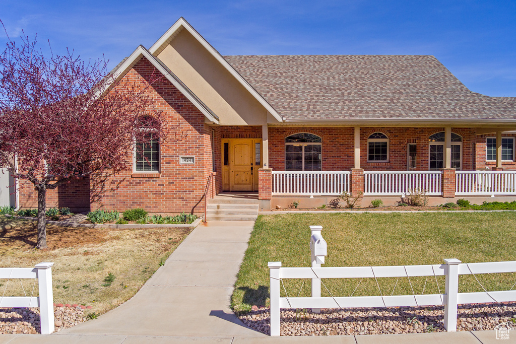 View of front facade featuring covered porch, a shingled roof, a front lawn, and brick siding