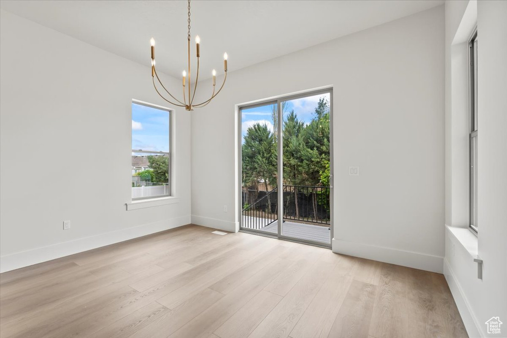 Empty room featuring a chandelier, plenty of natural light, light wood finished floors, and baseboards