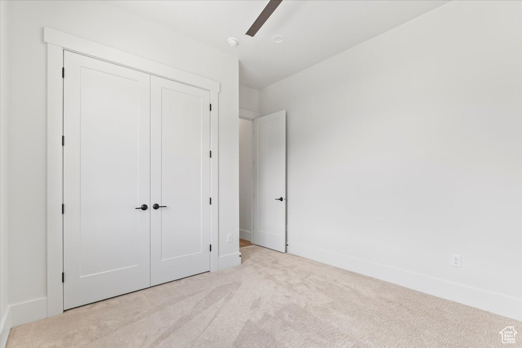 Unfurnished bedroom featuring light carpet, a closet, baseboards, and a ceiling fan