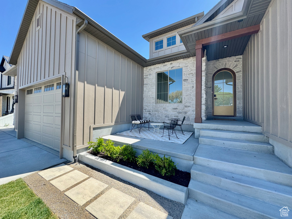 Entrance to property with board and batten siding, stone siding, driveway, and a garage