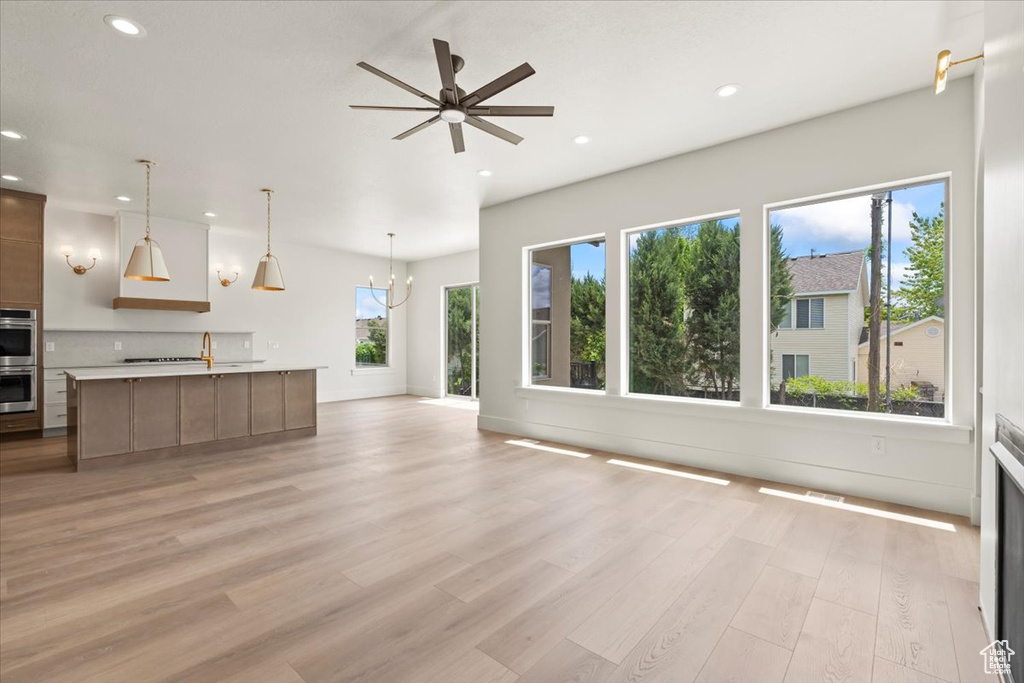 Unfurnished living room with recessed lighting, light wood-style flooring, ceiling fan, a chandelier, and baseboards