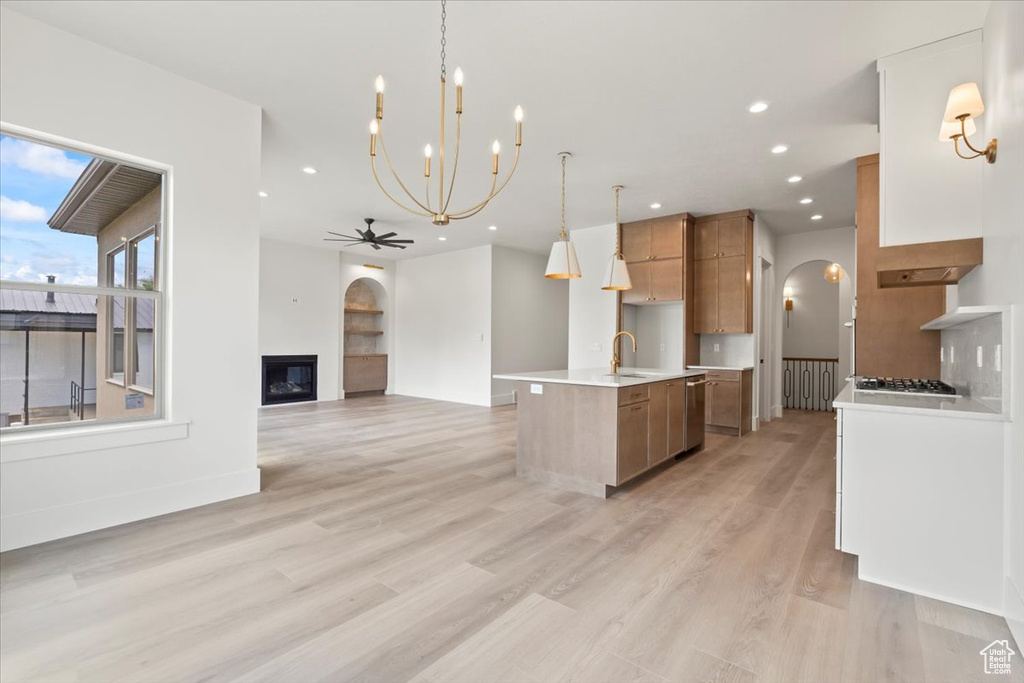 Kitchen with arched walkways, brown cabinets, a sink, appliances with stainless steel finishes, and a center island with sink