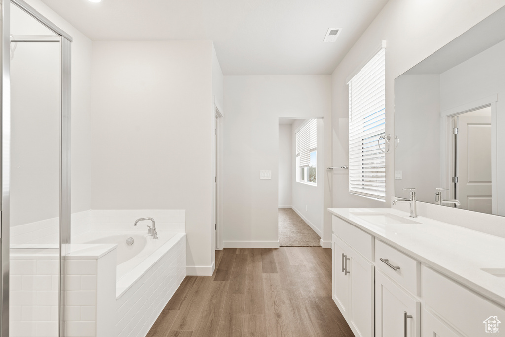 Full bath with wood finished floors, a bath, double vanity, baseboards, and a shower with door