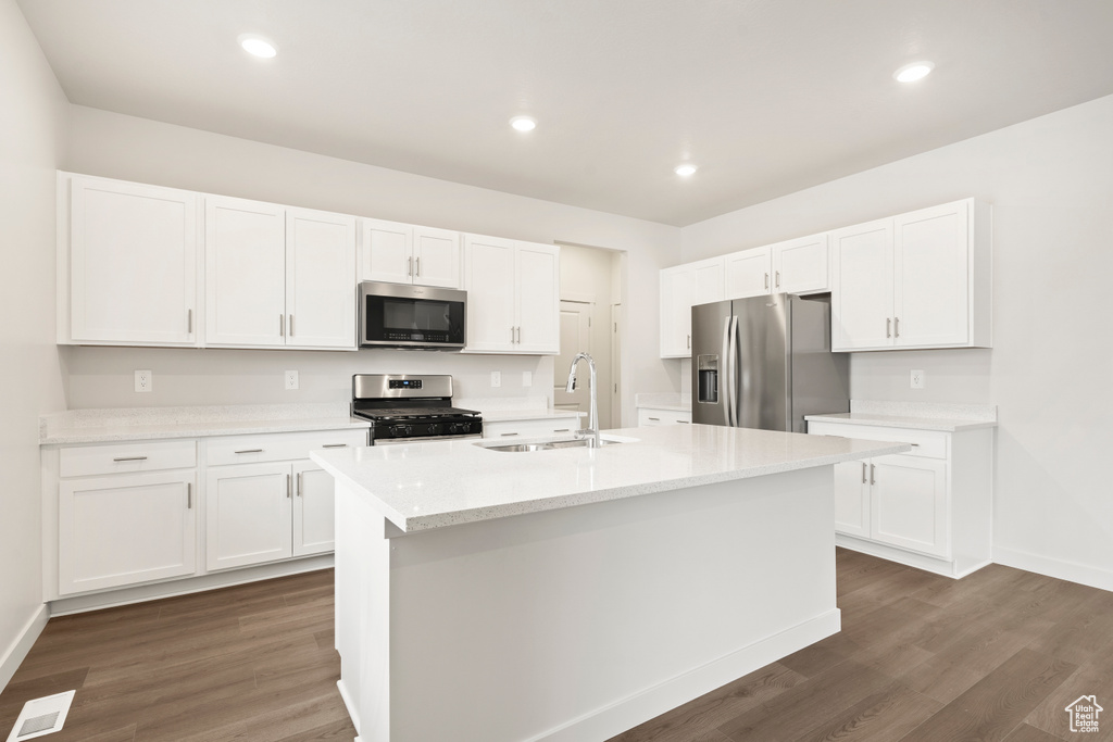 Kitchen with appliances with stainless steel finishes, a sink, white cabinetry, dark wood finished floors, and baseboards