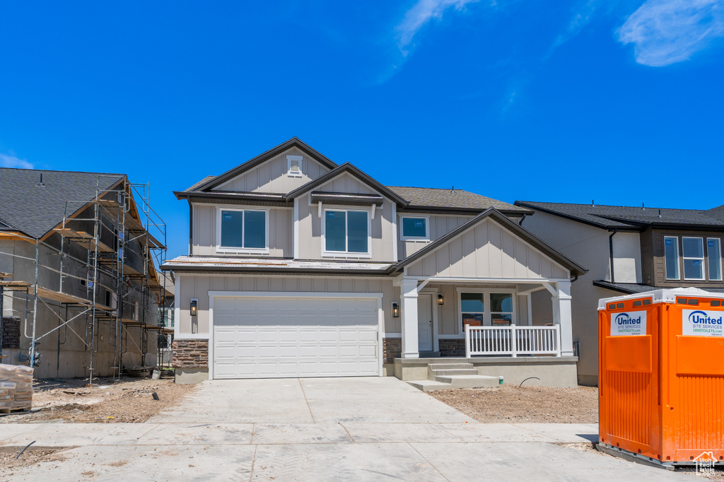 Craftsman-style house featuring a porch, driveway, an attached garage, board and batten siding, and stone siding