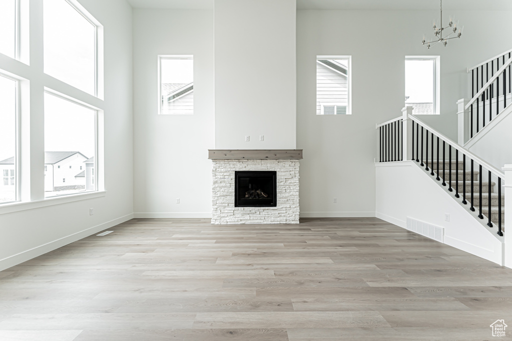 Unfurnished living room featuring stairs, a high ceiling, a chandelier, light wood-type flooring, and a stone fireplace