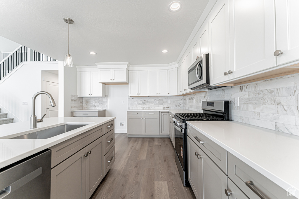 Kitchen with stainless steel appliances, gray cabinetry, pendant lighting, backsplash, and light countertops