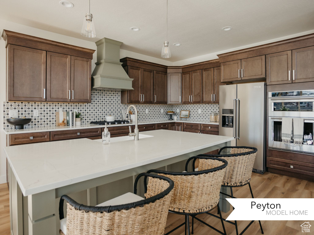 Kitchen with a kitchen breakfast bar, premium range hood, stainless steel appliances, backsplash, and light wood finished floors