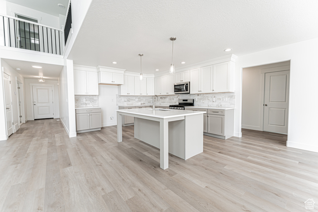 Kitchen featuring stainless steel appliances, backsplash, recessed lighting, a kitchen island with sink, and light countertops