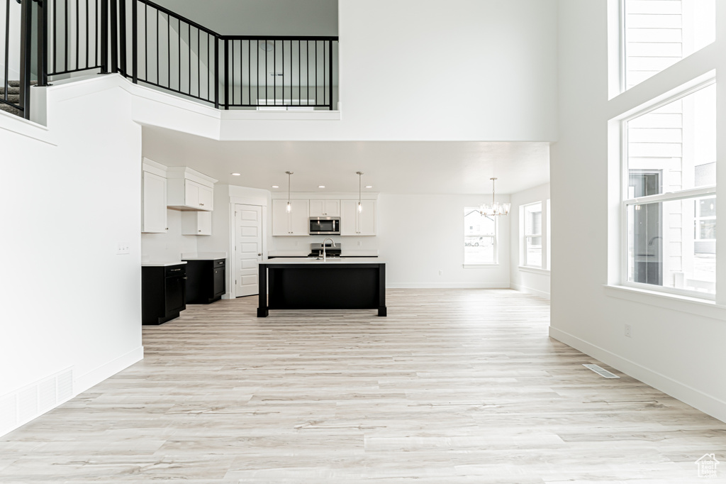 Unfurnished living room with a high ceiling, a chandelier, light wood-type flooring, and recessed lighting