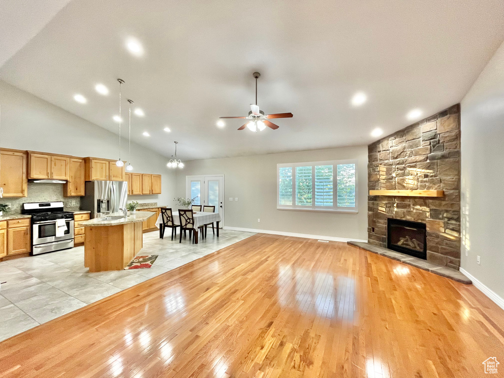 Kitchen featuring appliances with stainless steel finishes, open floor plan, a fireplace, an island with sink, and ceiling fan