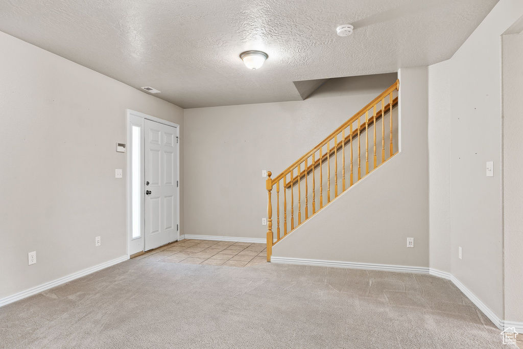 Foyer entrance with carpet floors, stairway, a textured ceiling, and baseboards