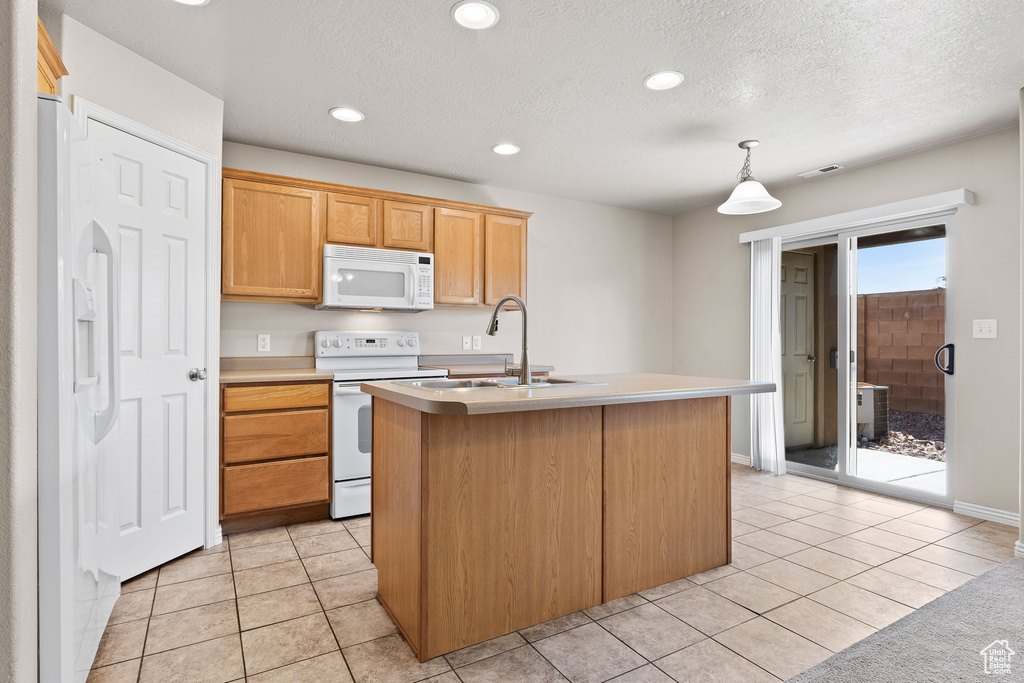 Kitchen with white appliances, a sink, light countertops, a center island with sink, and a textured ceiling