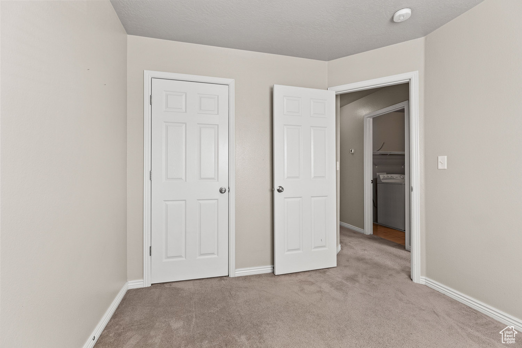 Unfurnished bedroom featuring carpet floors, baseboards, and washer / dryer