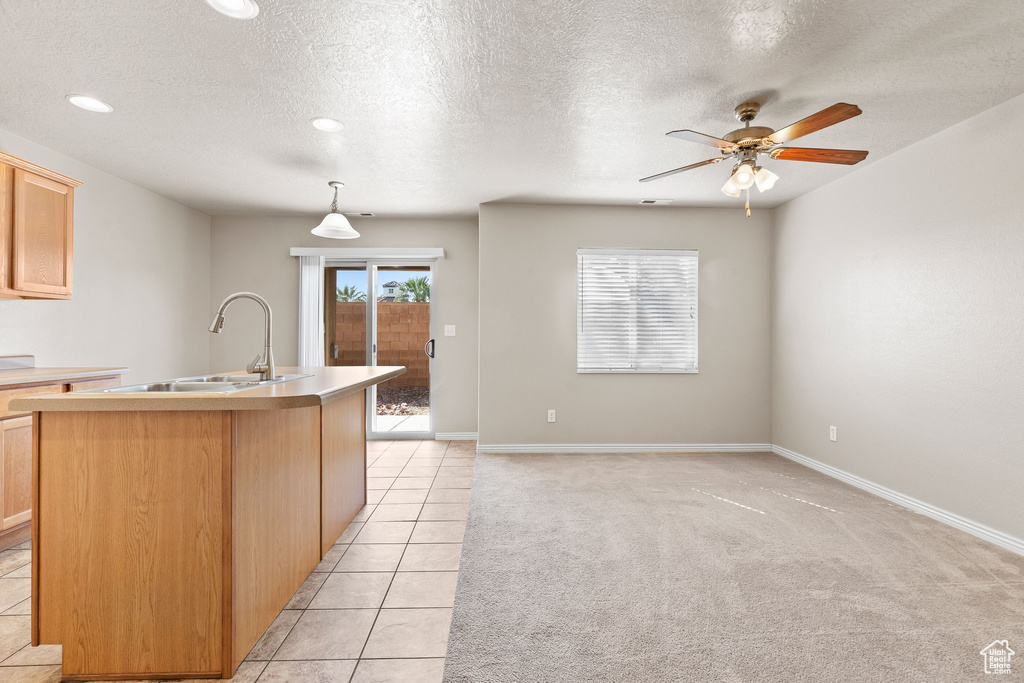 Kitchen with a sink, a ceiling fan, an island with sink, a textured ceiling, and light countertops