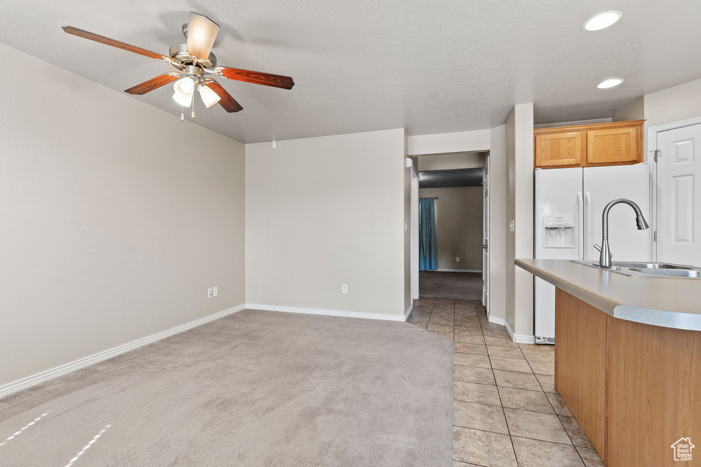 Kitchen with a sink, a ceiling fan, white fridge with ice dispenser, light countertops, and baseboards