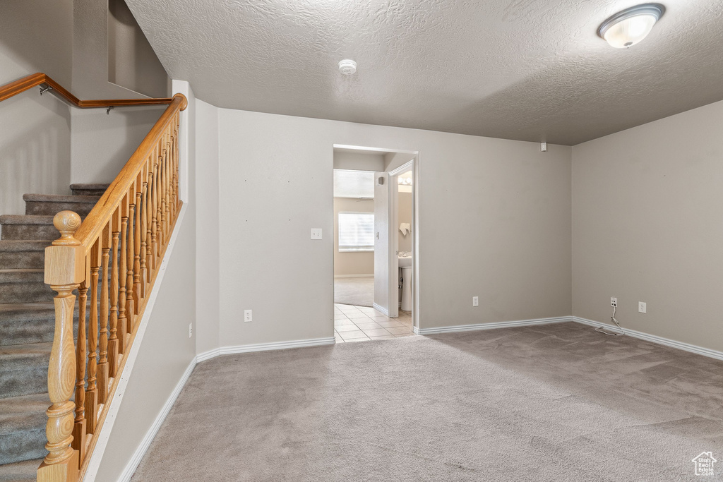 Empty room featuring carpet, a textured ceiling, baseboards, a smoke detector, and stairway