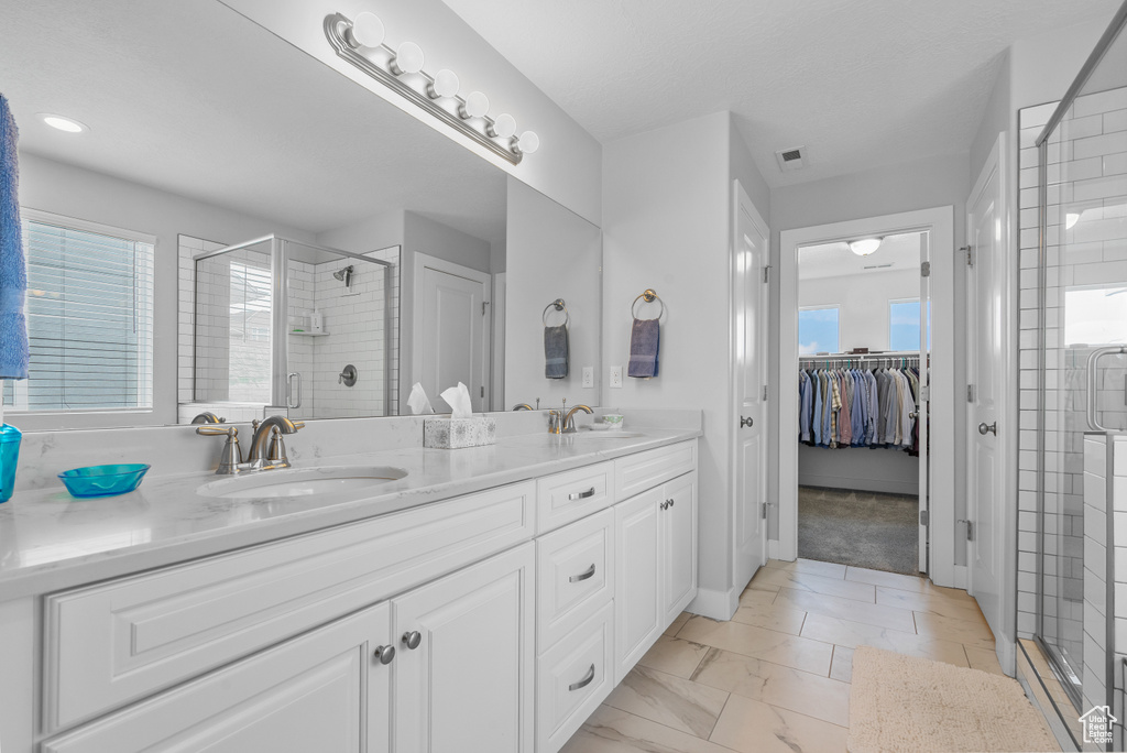 Bathroom featuring a shower stall, plenty of natural light, double vanity, and a spacious closet