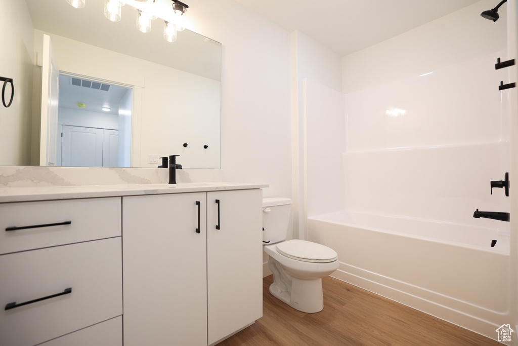 Bathroom with toilet, vanity, shower / tub combination, wood finished floors, and visible vents